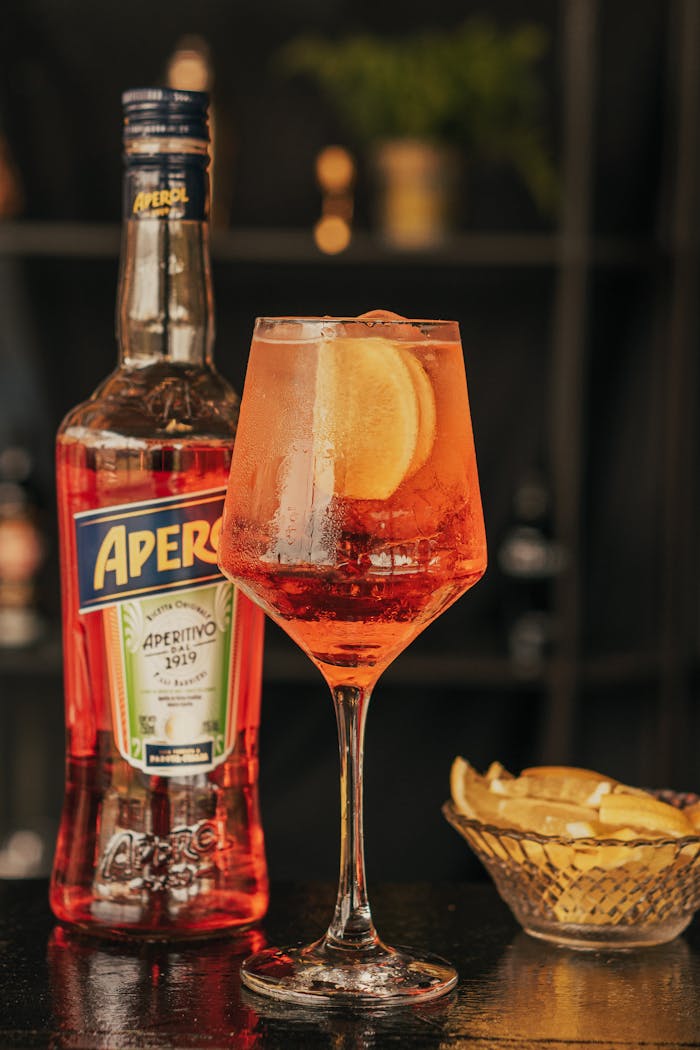about-us-01 Close-up of a classic Aperol Spritz with orange slice, featuring Aperol bottle and lemon wedges.